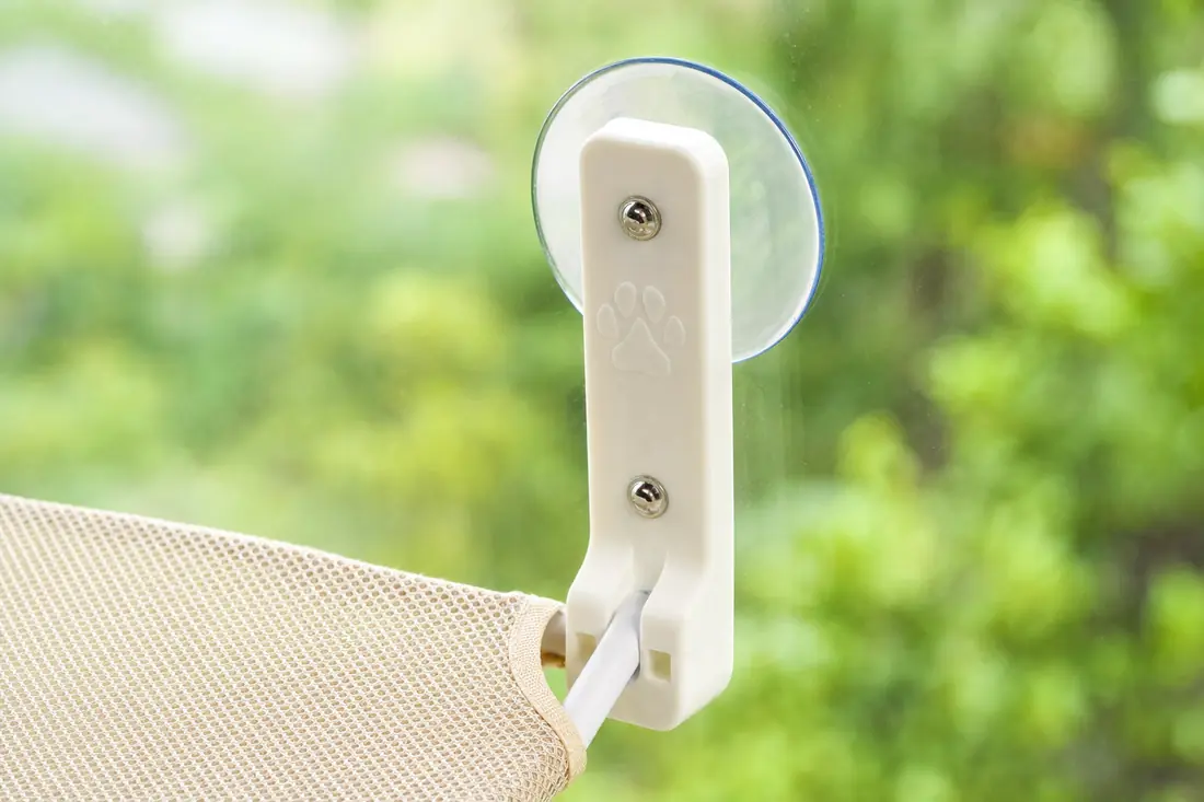 Gros plan d’une ventouse plaquée sur une vitre, bras blanc du hamac visible